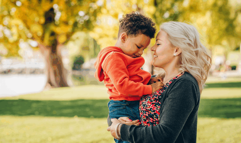 Middle-aged blonde woman holding her young African American song in a park on a fall day