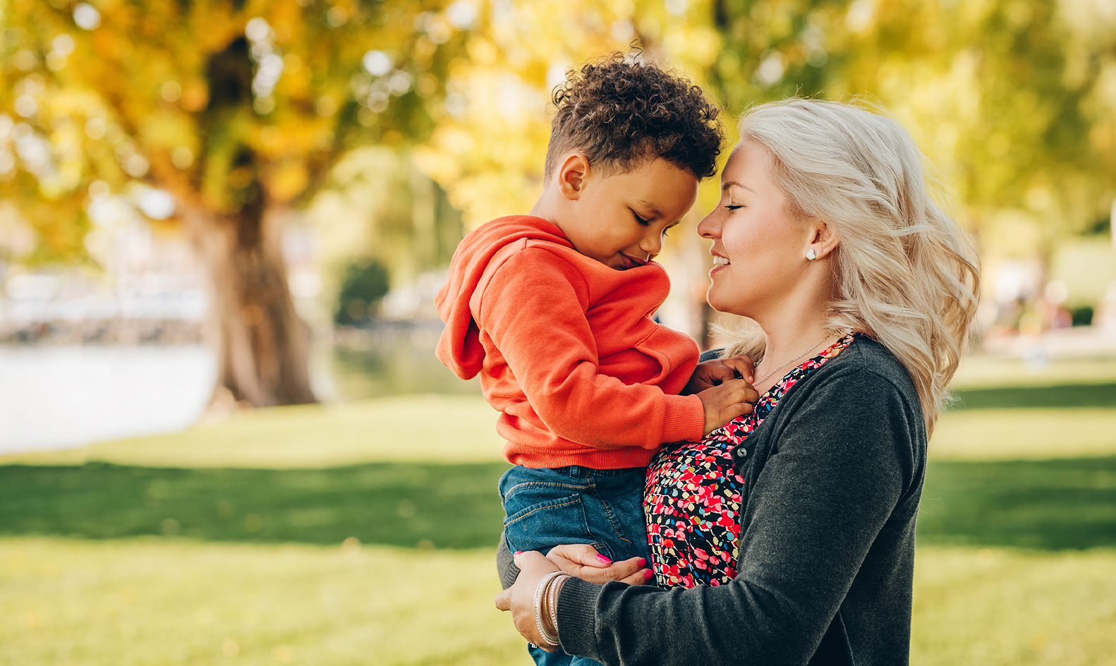 Middle-aged blonde woman holding her young African American song in a park on a fall day